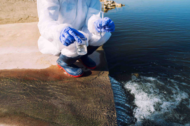 An image showing an ecologist standing where sewage wastewater meets the river and taking samples to determine the level of contamination and pollution.