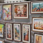 An image showing an outdoor art exhibition with framed cityscape paintings.