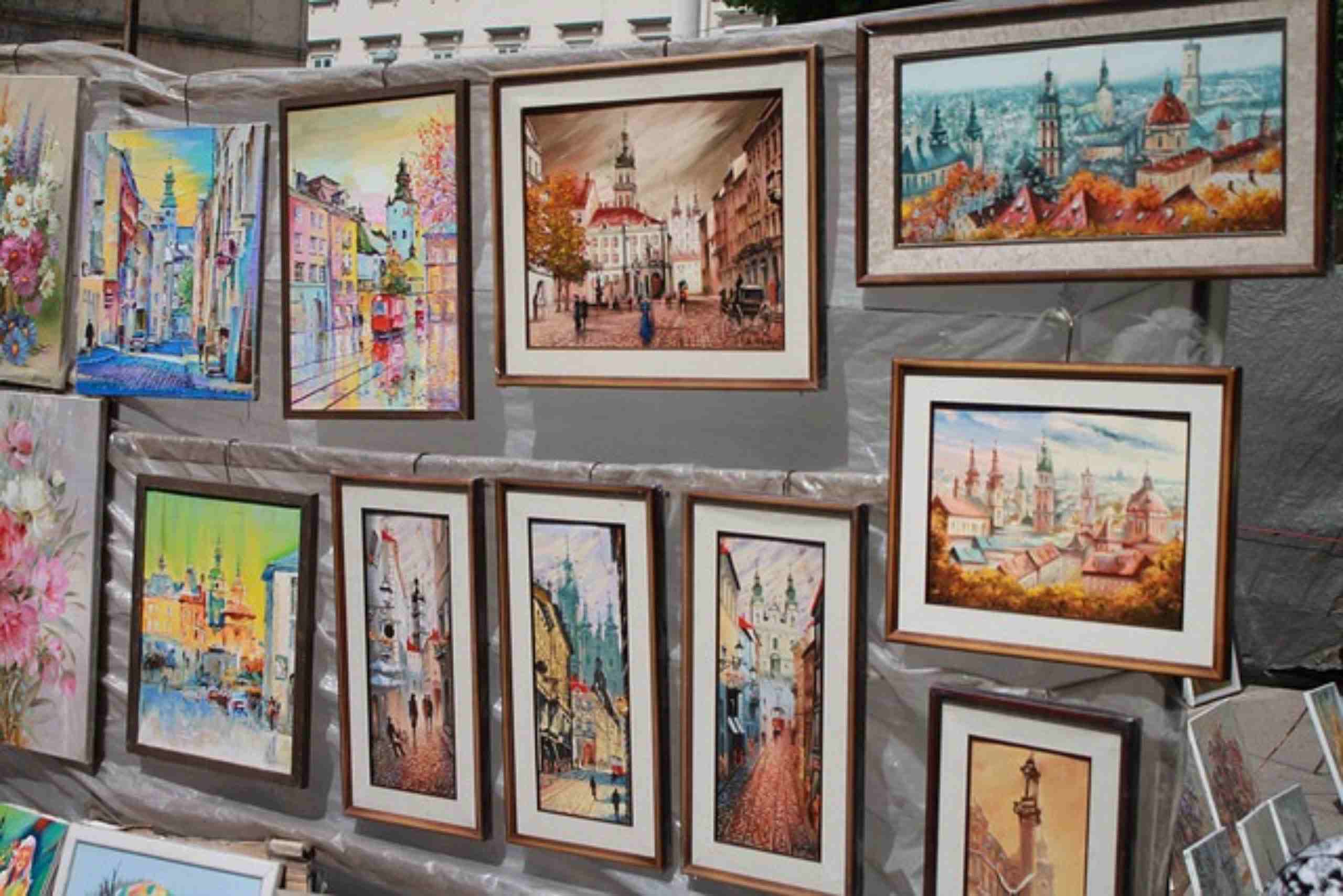 An image showing an outdoor art exhibition with framed cityscape paintings.