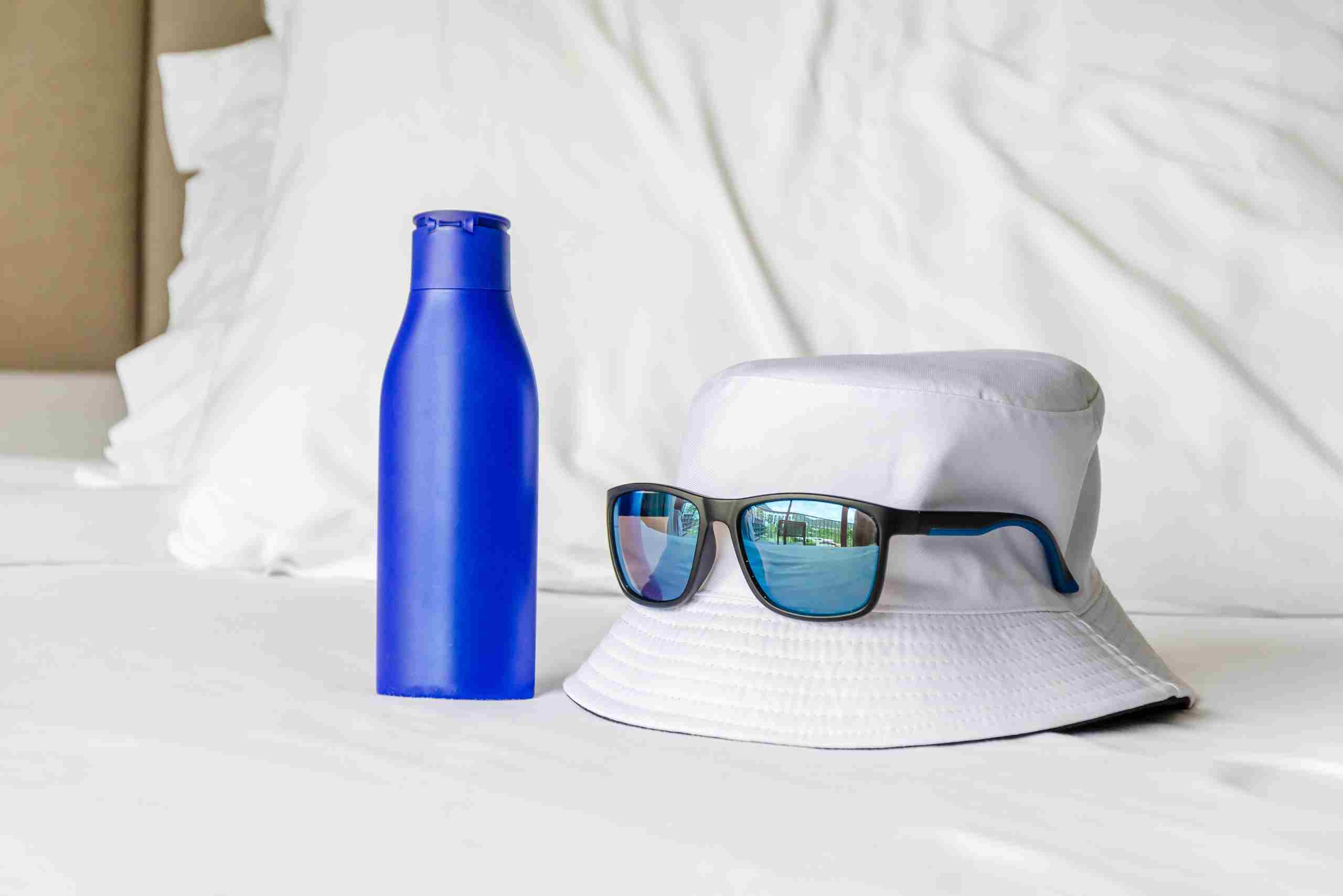 An image showing sun protection hiking materials including a hat, sunglasses, and UV cream.