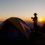 An image showing a man by his camping tent in the mountains, depicting camping in Lesotho.