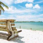 Brown wooden bench on white beach sand.